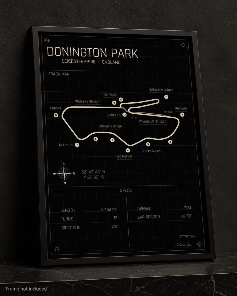 Op de afbeelding: Ingelijste print van het Donington Park circuit in Leicestershire, Engeland. De circuitkaart is wit op een zwarte achtergrond, met gelabelde bochten en een windroos. De print bevat circuitspecificaties.
