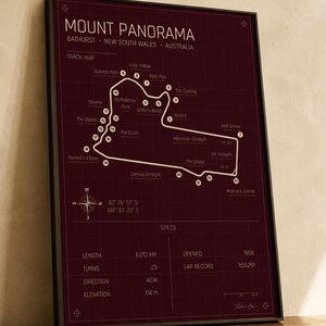 May include: A framed print of the Mount Panorama race track in Bathurst, New South Wales, Australia. The track map is white on a dark burgundy background. The print includes track details such as length, turns, and elevation. The frame is black.