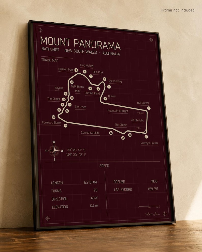 May include: A framed print of the Mount Panorama race track in Bathurst, New South Wales, Australia. The track map is white on a dark burgundy background. The print includes track details such as length, turns, and elevation. The frame is black.
