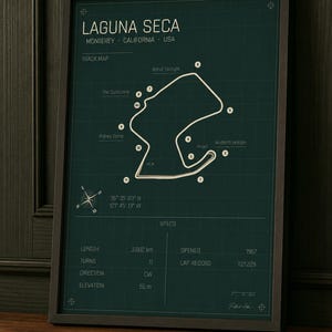 May include: Framed print of the Laguna Seca race track in Monterey, California. The track map is white on a dark green background, with the track's name and specifications. The frame is dark brown.