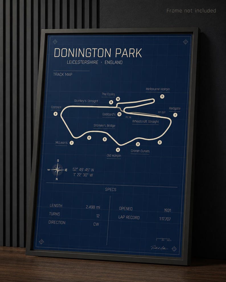 Op de afbeelding: Een ingelijste print in blauwdrukstijl van Donington Park, een racecircuit in Leicestershire, Engeland. De kaart van het circuit is wit op een donkerblauwe achtergrond, met gelabelde bochten en specificaties, waaronder een lengte van 4,02 km en een ronderecord van 1:17.707.