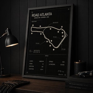 May include: Black framed print of the Road Atlanta race track in Braselton, Georgia, USA. The track map is white on a black background, with details including length, turns, and elevation. The print includes the text "Frame not included."