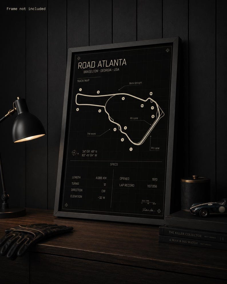 May include: Black framed print of the Road Atlanta race track in Braselton, Georgia, USA. The track map is white on a black background, with details including length, turns, and elevation. The print includes the text "Frame not included."