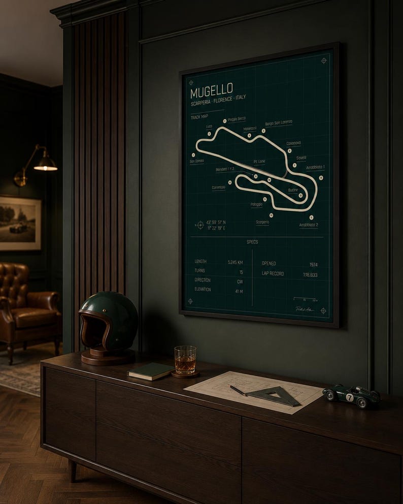 May include: A framed poster of the Mugello race track in Italy, with a dark green background and white track lines. A dark green helmet, a small green race car, and a glass of amber liquid sit on a dark wood cabinet.