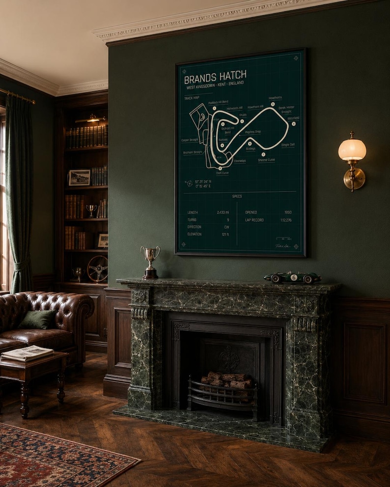 May include: A framed Brands Hatch race track map in a dark green room. The map is white on a dark green background. The room has a fireplace, a leather couch, and a bookshelf. A small model race car sits on the mantel.
