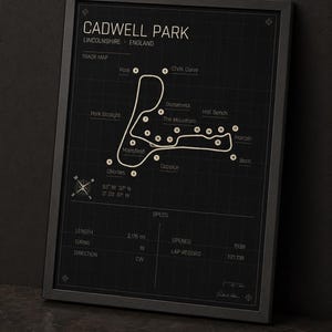 K&ouml;nnte beinhalten: Schwarz gerahmter Druck der Rennstrecke Cadwell Park in Lincolnshire, England. Die Streckenkarte ist wei&szlig; auf schwarzem Hintergrund, mit beschrifteten Kurven und Spezifikationen. Die Streckenl&auml;nge betr&auml;gt 3,5 km. Enth&auml;lt die Koordinaten der Strecke.