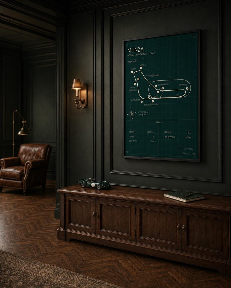 Op de afbeelding: Een ingelijste racekaart van het Monza circuit in Itali&euml;, op een donkergroene achtergrond. De witte kaart toont de baanindeling en details. Daaronder een donkerhouten kast met modelauto en boek. Donkere muren en een leren fauteuil.