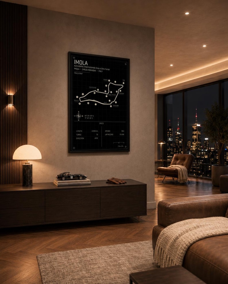 May include: A framed black and white Imola race track map hangs on a wall in a modern living room. The map includes the track layout, and the word "IMOLA" is at the top. A dark wood cabinet with a lamp and a model car sits below the map.