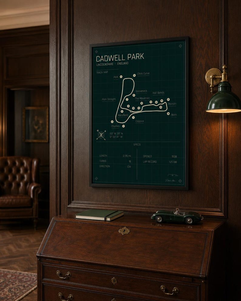 K&ouml;nnte beinhalten: Gerahmter Cadwell Park Streckenplan, Lincolnshire, England, in dunklem Gr&uuml;n und Wei&szlig;. Der Druck wird an einer dunklen Holzwand &uuml;ber einem Holzschreibtisch angezeigt. Ein gr&uuml;nes Spielzeugauto und ein gr&uuml;nes Notizbuch liegen auf dem Schreibtisch.