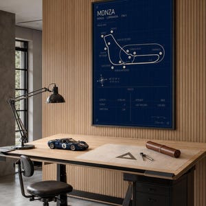 Op de afbeelding: Een ingelijste blauwdruk-stijl poster van het Monza circuit in Itali&euml;, met een donkerblauwe achtergrond en witte lijnen. Een klein blauw racewagenmodel staat op een houten bureau, samen met tekengereedschap en een bureaulamp.