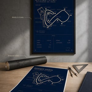 May include: A framed Brands Hatch track map poster in a black frame, with a rolled poster and print on a wooden surface. The poster is blue with white lines and text, including track details and specs. The text includes "Brands Hatch" and "West Kingsdown - Kent - England".