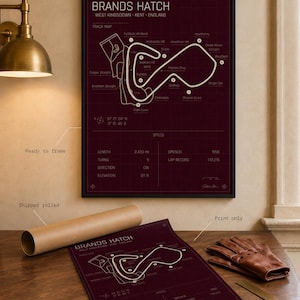 May include: A framed burgundy print of the Brands Hatch race track in West Kingsdown, Kent, England. The track map is in white, with text including track details and specs. A rolled print and leather gloves are also visible.