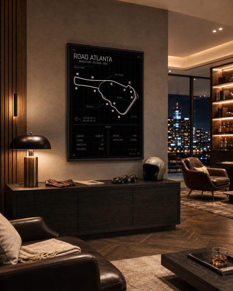 May include: A framed black and white print of the Road Atlanta racetrack map hangs above a dark wood cabinet. A vintage racing helmet and a model race car sit on the cabinet. A lamp with a gold base and black shade is on the left.