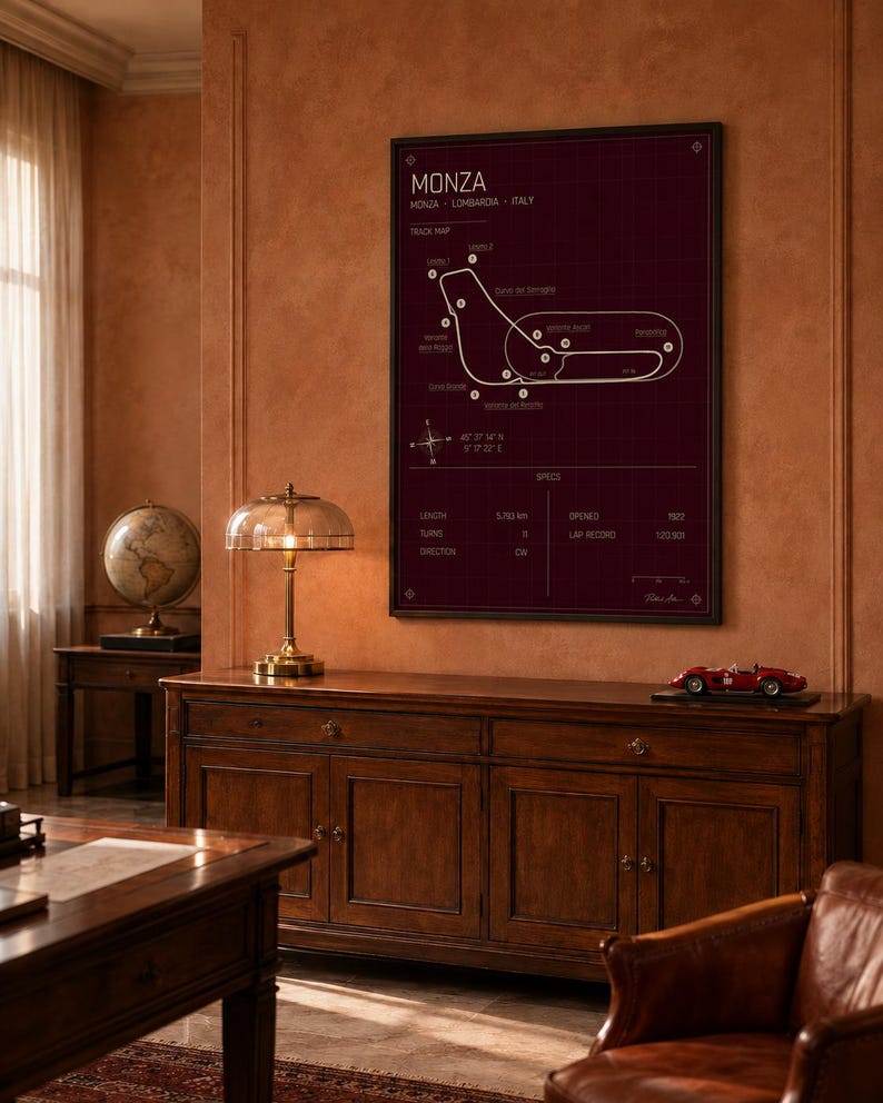 Op de afbeelding: Een ingelijste print van het Monza-circuit in Itali&euml;, met een witte circuitkaart op een donkerrode achtergrond. De print bevat circuitspecificaties en wordt weergegeven boven een houten kast met een modelraceauto.