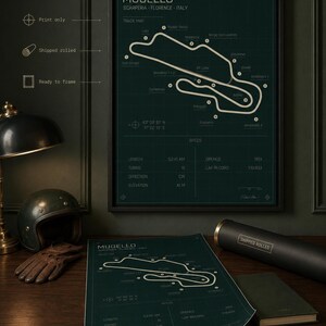 May include: A framed print of the Mugello race track in Italy, with a detailed track map and specifications. The print is in a black frame, with a dark green background and white text. A rolled print and a helmet are also visible.