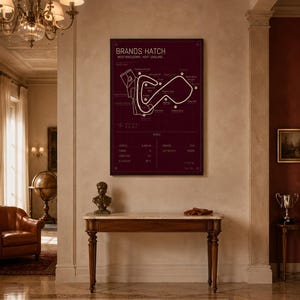 May include: A framed burgundy print of the Brands Hatch race track in West Kingsdown, Kent, England. The track map is white, with text at the top and bottom. The print hangs on a beige wall above a wooden table.