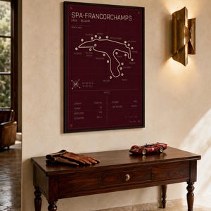 Pode incluir: Um mapa do circuito de Spa-Francorchamps emoldurado em bord&ocirc;, com moldura preta, pendurado acima de uma mesa de madeira escura. Na mesa, luvas de couro marrom e um modelo de carro de corrida vermelho. Arandela dourada.