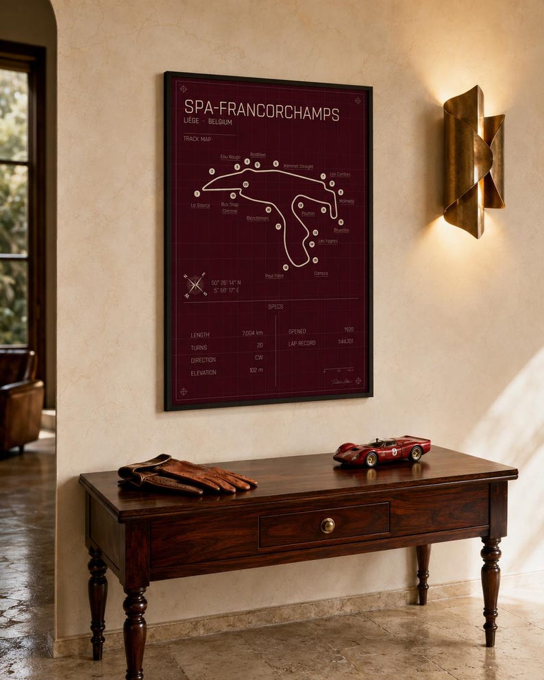 Pode incluir: Um mapa do circuito de Spa-Francorchamps emoldurado em bord&ocirc;, com moldura preta, pendurado acima de uma mesa de madeira escura. Na mesa, luvas de couro marrom e um modelo de carro de corrida vermelho. Arandela dourada.