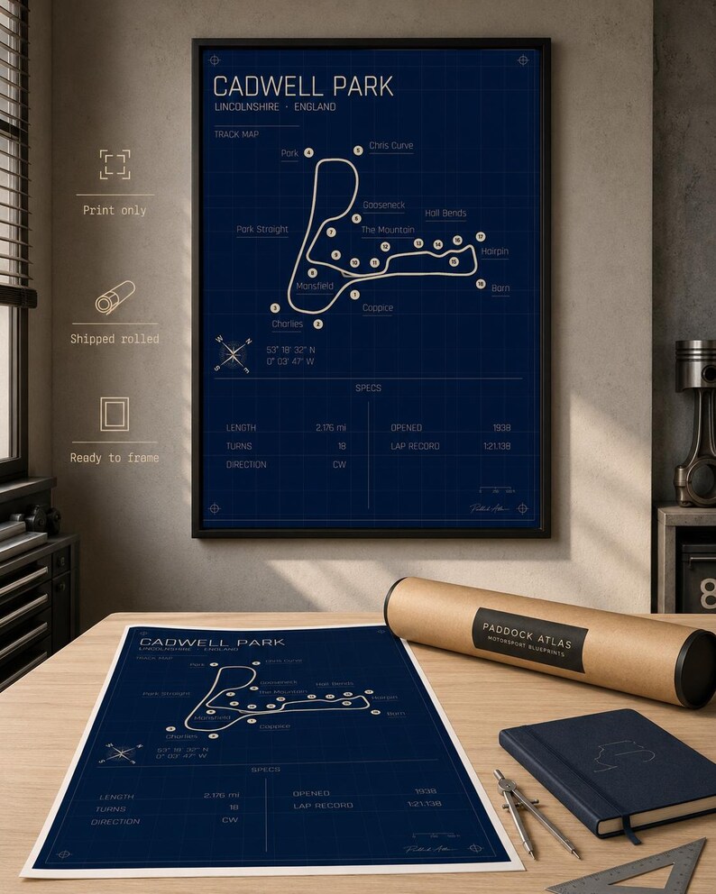K&ouml;nnte beinhalten: Gerahmter Cadwell Park Streckenplan-Druck in Marineblau mit wei&szlig;em Text und Rasterhintergrund. Der Druck enth&auml;lt Streckendetails und Spezifikationen. Eine gerollte Druck, ein Notizbuch und Zeichenwerkzeuge liegen auf dem Tisch.