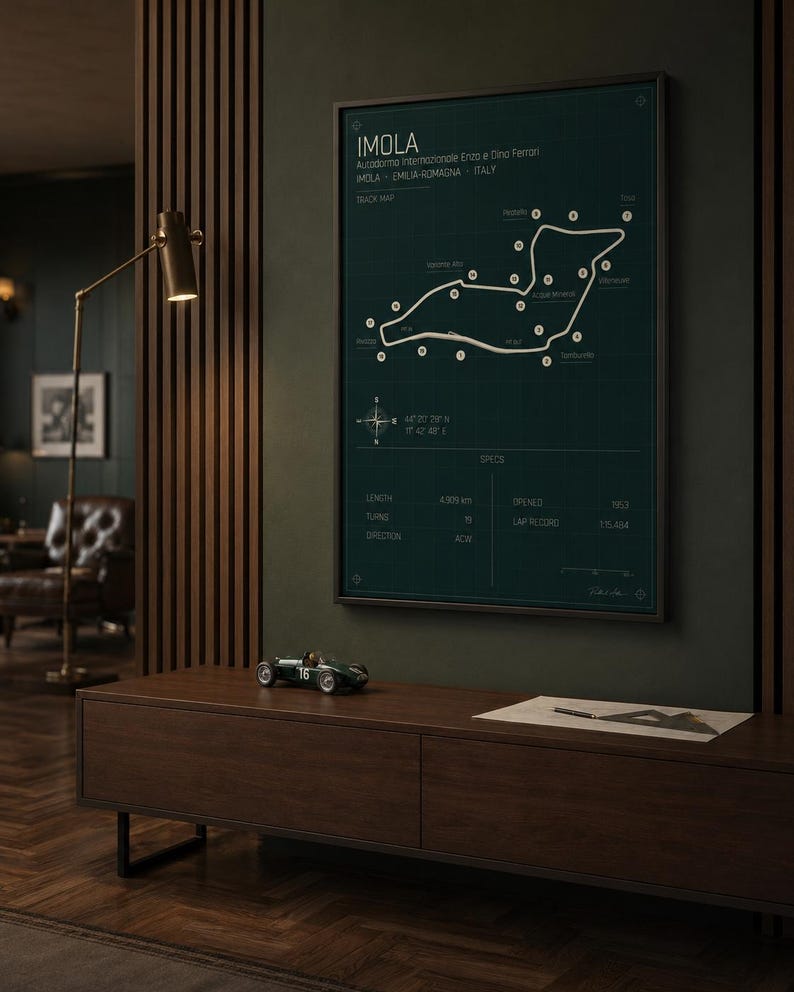 May include: A framed Imola race track map in a dark green hue, with white track lines and text. A small green race car model sits on a dark wood cabinet below the framed map. The text on the map includes "IMOLA" and track specifications.