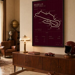 May include: A framed print of the Mugello race track map in white on a burgundy background. The print is displayed above a wooden cabinet with a red race car model, a vintage helmet, and a desk lamp. The print includes the track's length, turns, and elevation.