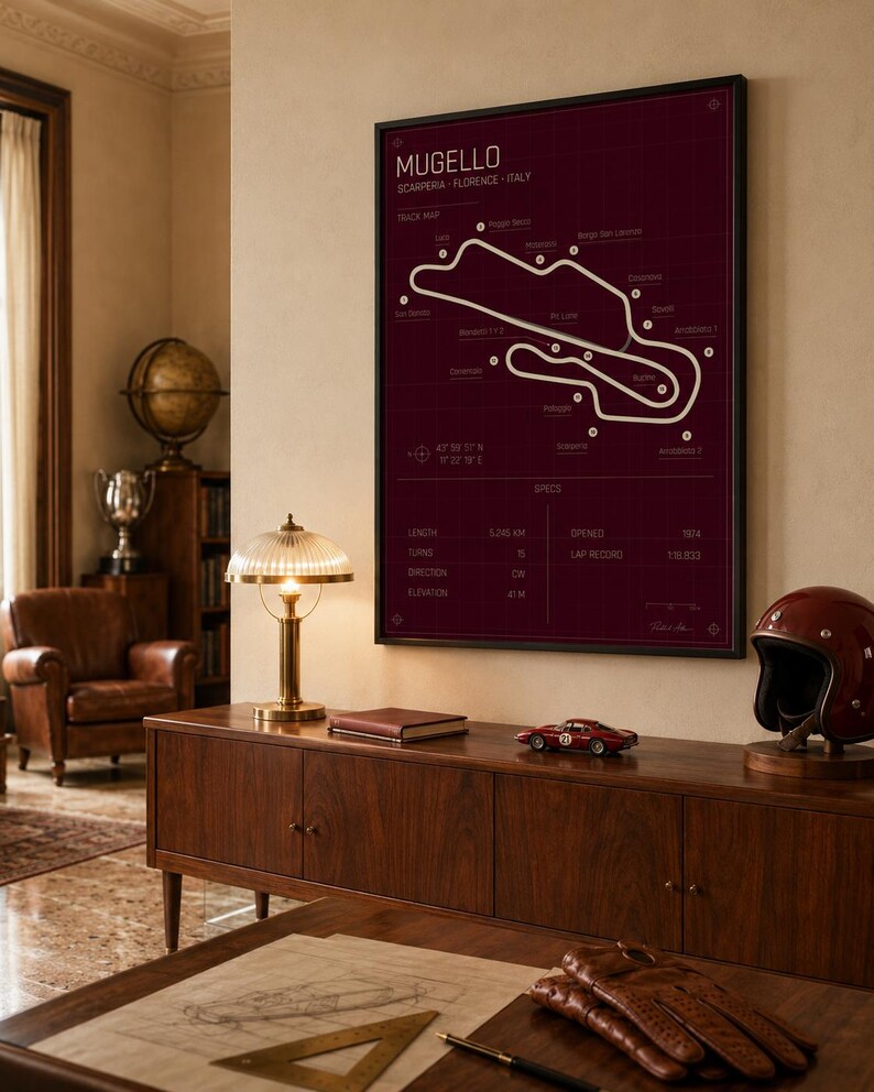 May include: A framed print of the Mugello race track map in white on a burgundy background. The print is displayed above a wooden cabinet with a red race car model, a vintage helmet, and a desk lamp. The print includes the track's length, turns, and elevation.