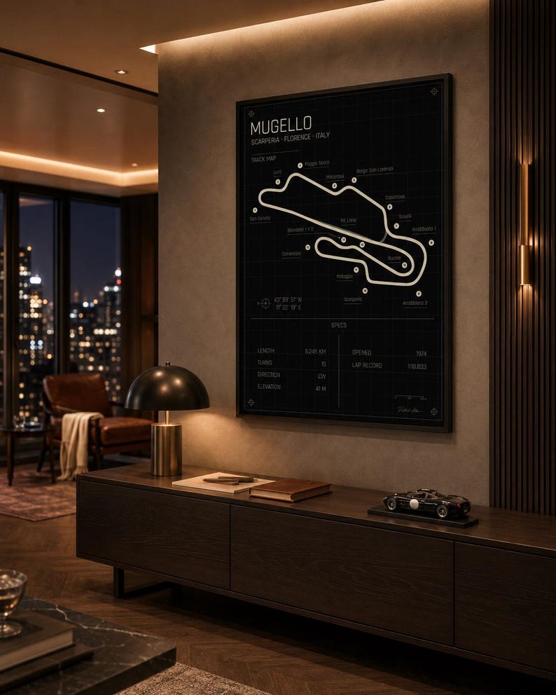 May include: A framed black and white track map of the Mugello circuit in Italy. The poster includes track details and is displayed above a dark wood cabinet. A small model race car sits on the cabinet.