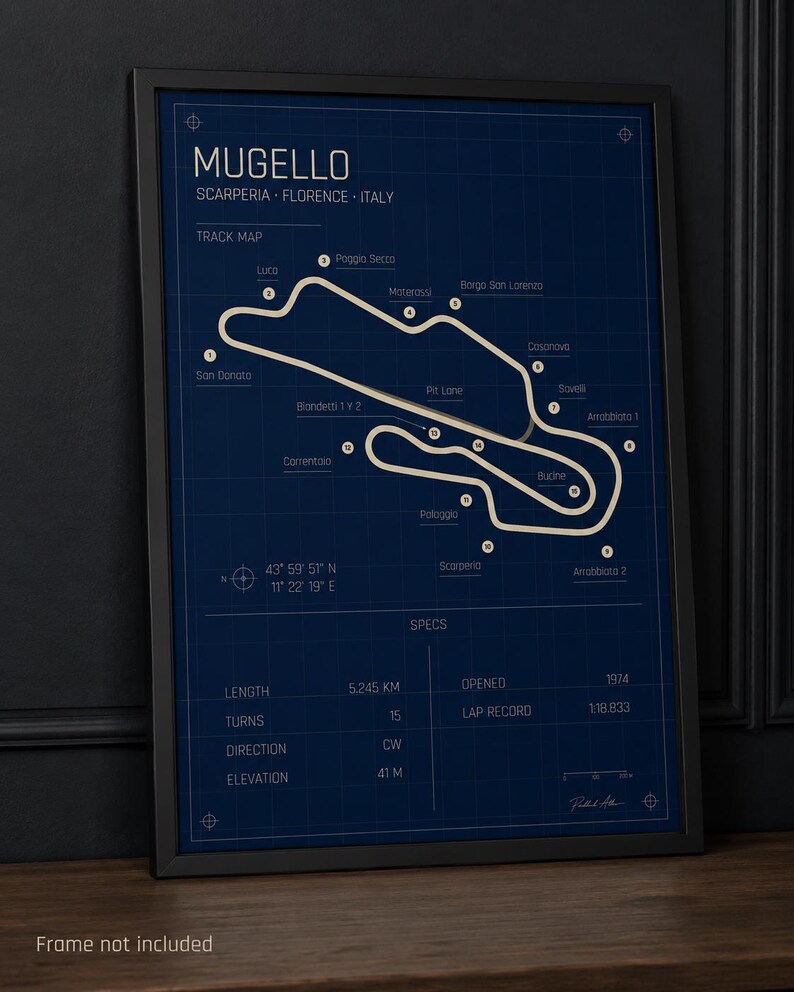 May include: A framed track map of the Mugello circuit in Italy. The map is white on a dark blue background, with the track layout and names of turns and sections. The frame is black. The map includes specs such as length (5.245 km) and turns (15).