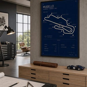 May include: A framed blueprint-style print of the Mugello race track in Italy, with the track layout in white against a dark blue background. The print includes track specifications and is displayed above a wooden cabinet. A small blue race car model sits on the cabinet.