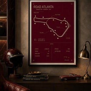 May include: A framed print of the Road Atlanta race track in Braselton, Georgia, USA. The track map is in white on a burgundy background. The print includes track specifications and is displayed with a vintage helmet, books, and a model car.