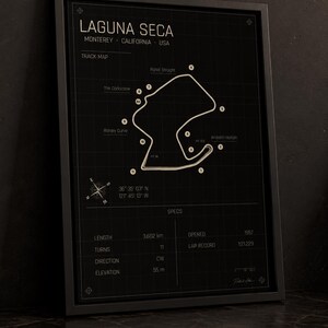 May include: Black framed print of the Laguna Seca racetrack in Monterey, California. The track map is white on a black background, with labeled turns and specs including length (3.602 km), turns (11), and elevation (55 m).