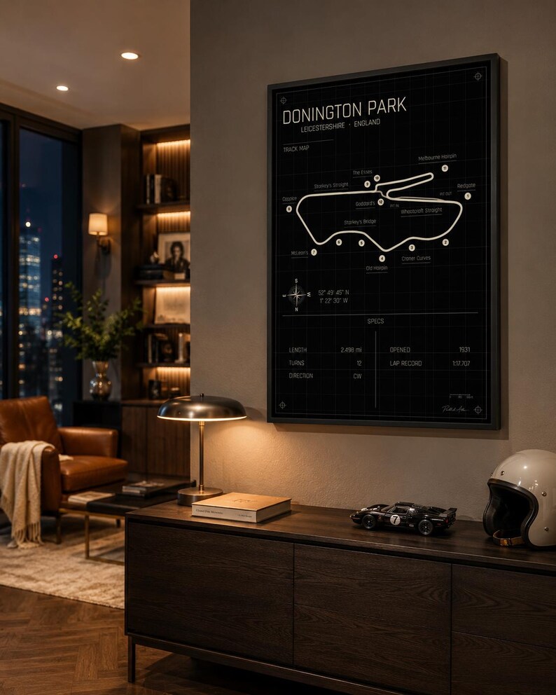 Op de afbeelding: Een zwart-wit afdruk van het Donington Park circuit in Leicestershire, Engeland. De afdruk toont een circuitkaart en specificaties. De afdruk hangt in een moderne woonkamer met houten meubels.