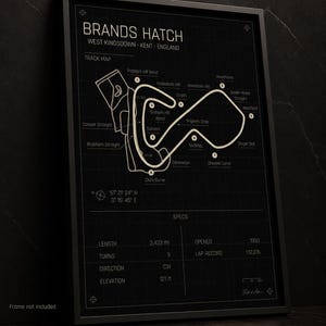 May include: Black framed Brands Hatch track map poster. The track map is in a light beige color, with the track layout and names of the turns. The poster includes specs such as length, turns, direction, and elevation. The text "Frame not included" is at the bottom.