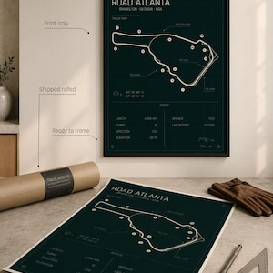 May include: A framed dark green print of the Road Atlanta race track in Braselton, Georgia, USA. The print includes track details and specifications. A rolled print and other items are on a table.