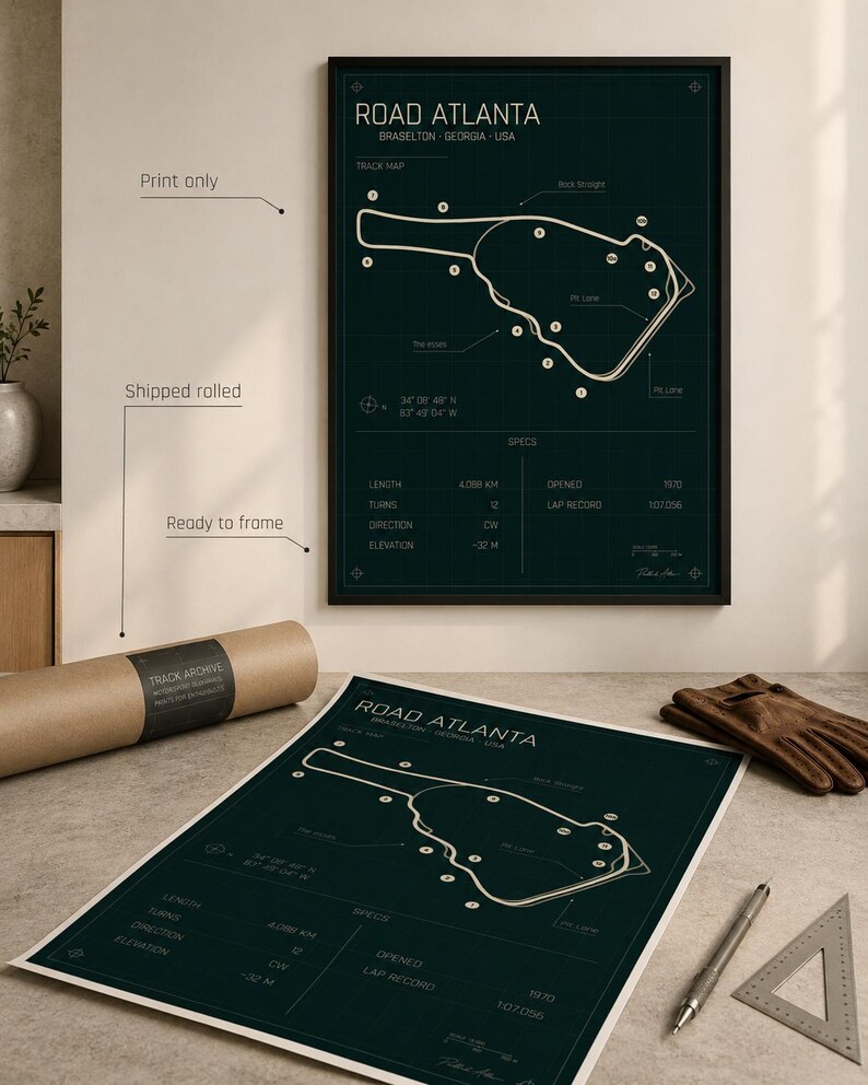 May include: A framed dark green print of the Road Atlanta race track in Braselton, Georgia, USA. The print includes track details and specifications. A rolled print and other items are on a table.