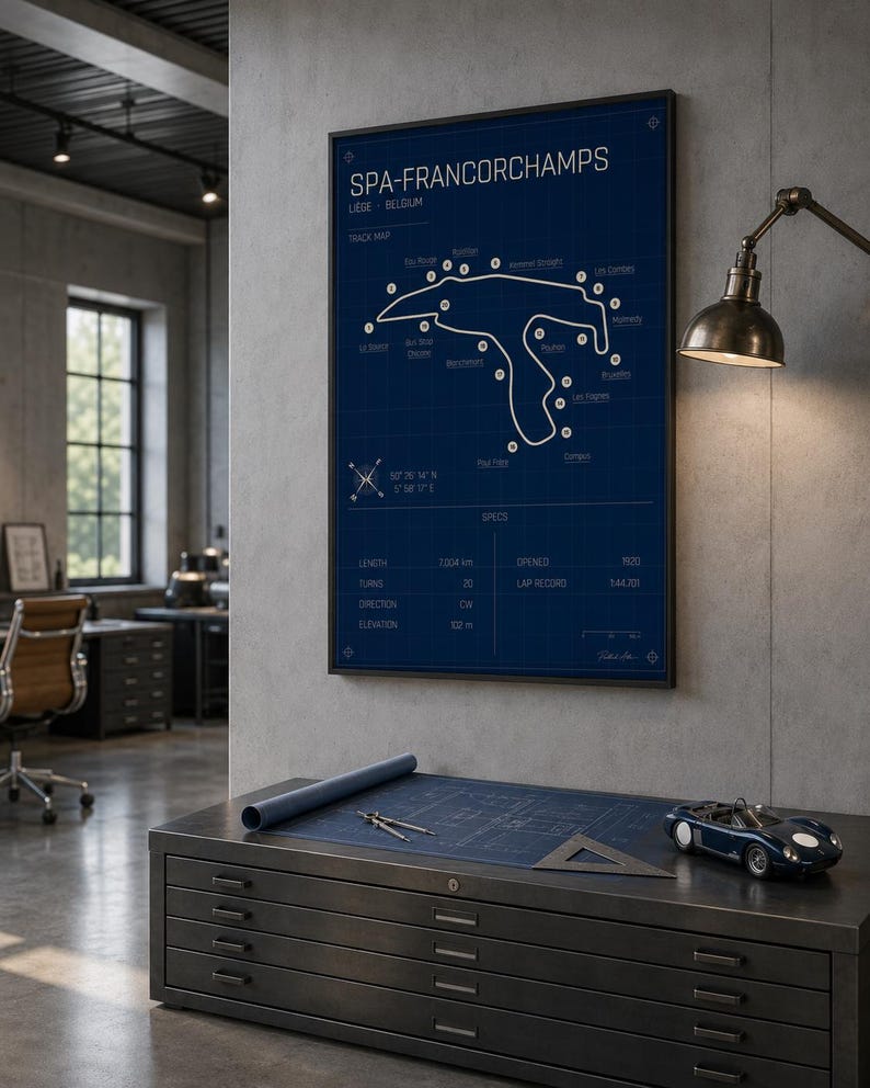 Pode incluir: Uma planta emoldurada do circuito de Spa-Francorchamps na B&eacute;lgica. O mapa da pista &eacute; branco sobre um fundo azul, com o texto "SPA-FRANCORCHAMPS" no topo. Um pequeno carro de brinquedo azul est&aacute; em um arm&aacute;rio de metal.