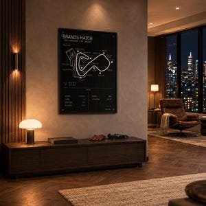 May include: A black framed Brands Hatch race track map poster hangs on a wall. The poster is above a dark wood cabinet with a lamp, a book, gloves, and a small car model. The room has a modern design with a city view.