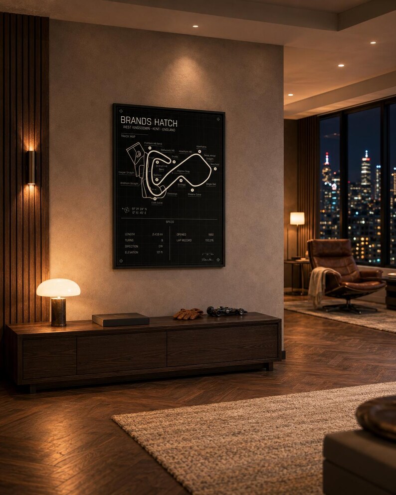 May include: A black framed Brands Hatch race track map poster hangs on a wall. The poster is above a dark wood cabinet with a lamp, a book, gloves, and a small car model. The room has a modern design with a city view.