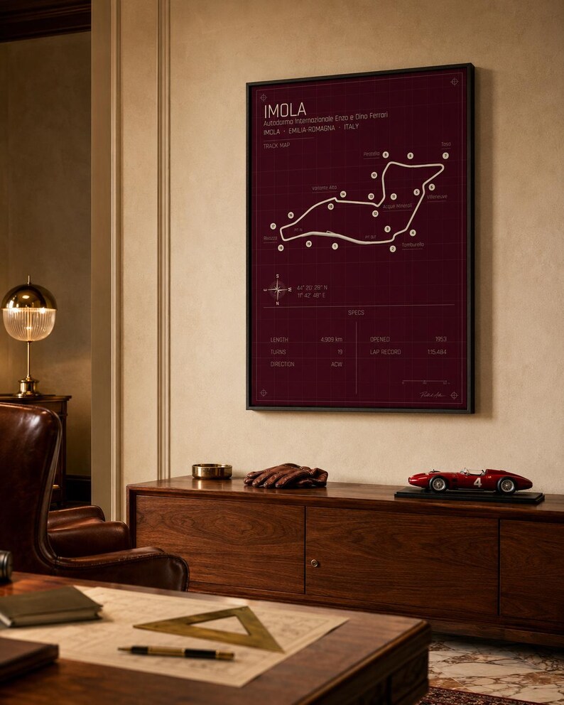May include: A framed Imola race track map in a dark burgundy color, with white lines and text. The track map is displayed above a wooden cabinet with a red race car model. The text on the map includes "IMOLA" and "TRACK MAP".