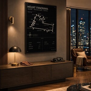 May include: A framed black and white Mount Panorama track map. The track map is displayed above a dark wood cabinet with a lamp, gloves, and a model car. The room has a modern design with a city view.