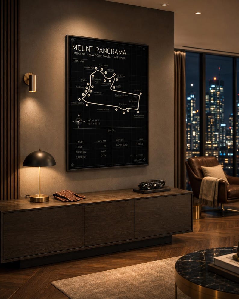 May include: A framed black and white Mount Panorama track map. The track map is displayed above a dark wood cabinet with a lamp, gloves, and a model car. The room has a modern design with a city view.