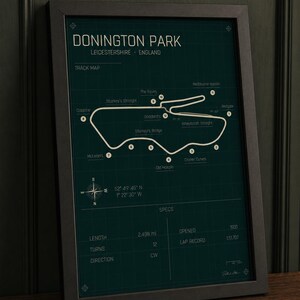 Op de afbeelding: Ingelijste print van het Donington Park circuit in Leicestershire, Engeland. De kaart is wit op een donkergroene achtergrond. Inclusief details zoals lengte, bochten en ronderecord. De lijst is zwart.