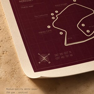 May include: A maroon and white track map print of Laguna Seca, California. The print includes the track layout, labeled features like "The Corkscrew" and "Rainey Curve", and coordinates. The paper is museum-quality matte, 250 gsm, archival, and acid-free.