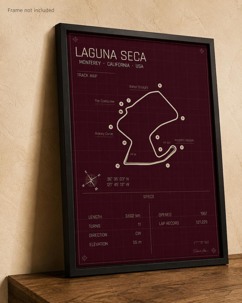 May include: Framed print of the Laguna Seca racetrack in Monterey, California, USA. The track map is white on a burgundy background, with details including length (3.602 km), turns (11), and elevation (55 m). The frame is black.