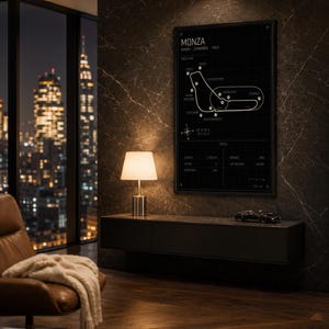 Op de afbeelding: Een zwart-wit afdruk met een kader van de Monza-racebaan, met de tekst "MONZA" bovenaan. De afdruk hangt boven een donkergrijze zwevende kast met een kleine modelauto erop. Een lamp met een witte kap staat op de kast.