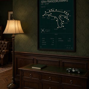 Pode incluir: Um poster emoldurado do mapa da pista de Spa-Francorchamps em verde escuro. O poster inclui detalhes e especifica&ccedil;&otilde;es da pista. Um carro de corrida verde e um livro est&atilde;o em um arm&aacute;rio de madeira. Uma lumin&aacute;ria de ch&atilde;o com uma abajur bege est&aacute; &agrave; esquerda.