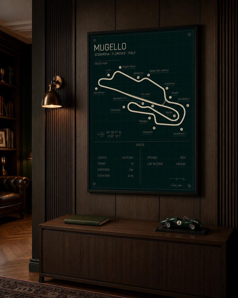 May include: A framed track map of the Mugello circuit in Scarperia, Florence, Italy, with a dark green background and white track lines. The map includes specifications such as length, turns, and elevation. A green model car sits on a wooden cabinet below.