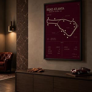 May include: Framed print of the Road Atlanta racetrack in Braselton, Georgia, USA. The track map is white on a burgundy background, with specifications listed below. A model race car and driving gloves sit on a dark wood cabinet.