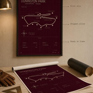 Op de afbeelding: Een ingelijste bordeauxrode print van het Donington Park circuit in Leicestershire, Engeland. De circuitkaart is wit, met details zoals lengte, bochten en richting. Een opgerolde print van hetzelfde ontwerp is ook zichtbaar.