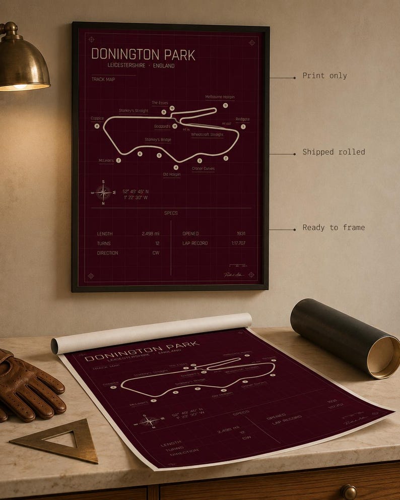 Op de afbeelding: Een ingelijste bordeauxrode print van het Donington Park circuit in Leicestershire, Engeland. De circuitkaart is wit, met details zoals lengte, bochten en richting. Een opgerolde print van hetzelfde ontwerp is ook zichtbaar.